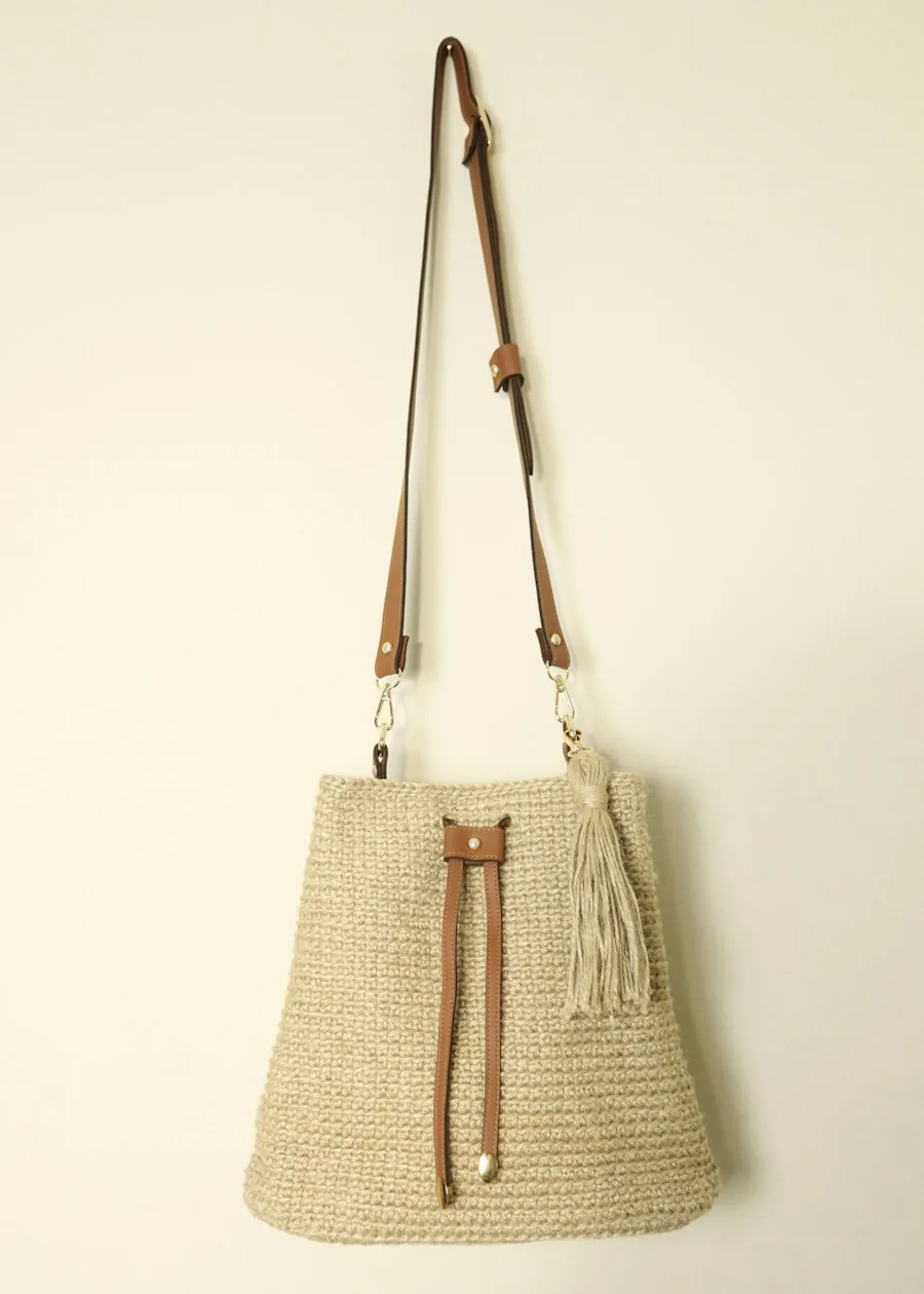Woven tote bag with a leather strap hanging on a wall