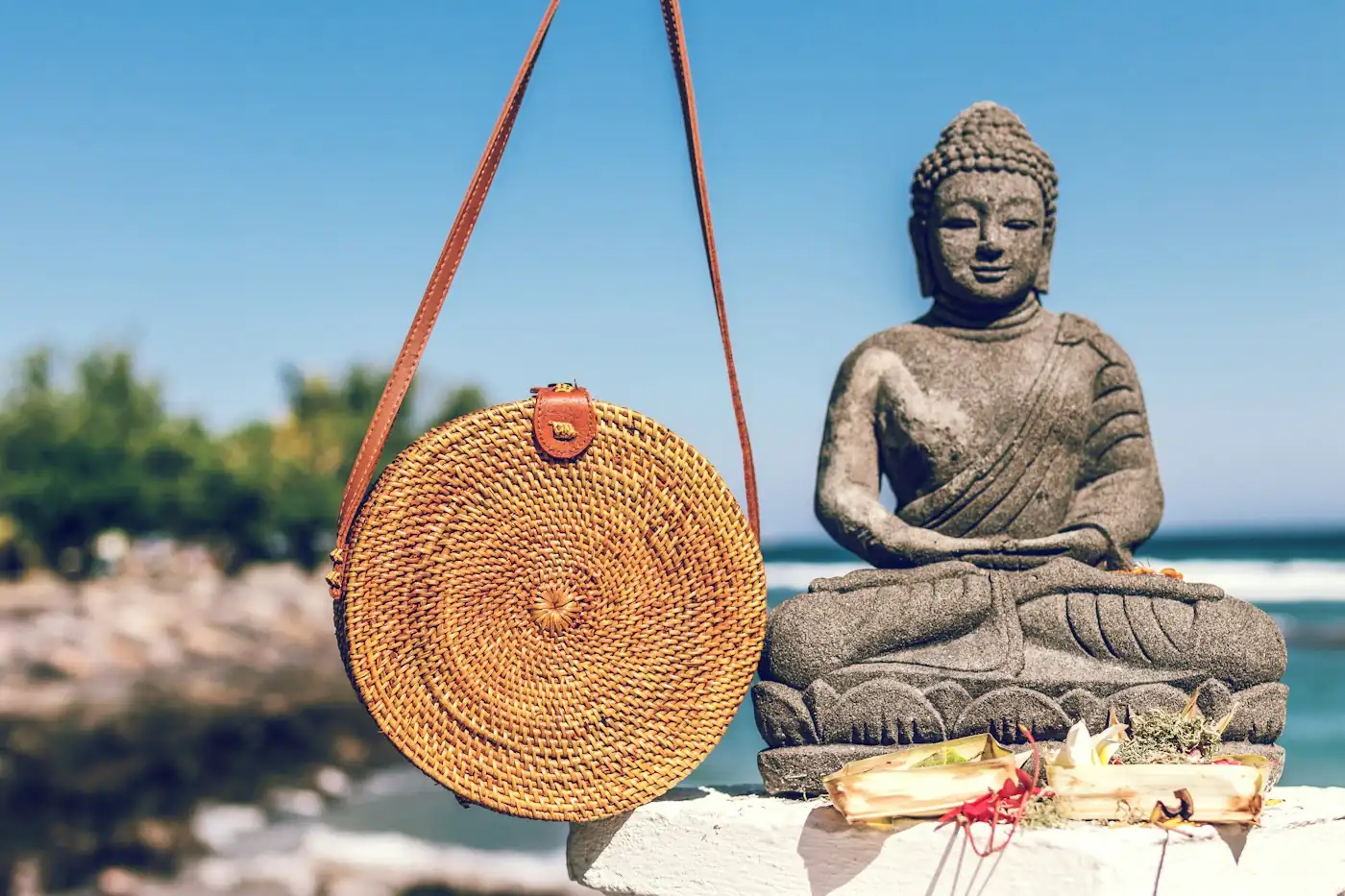 Round rattan bag hanging beside a stone Buddha statue in Bali