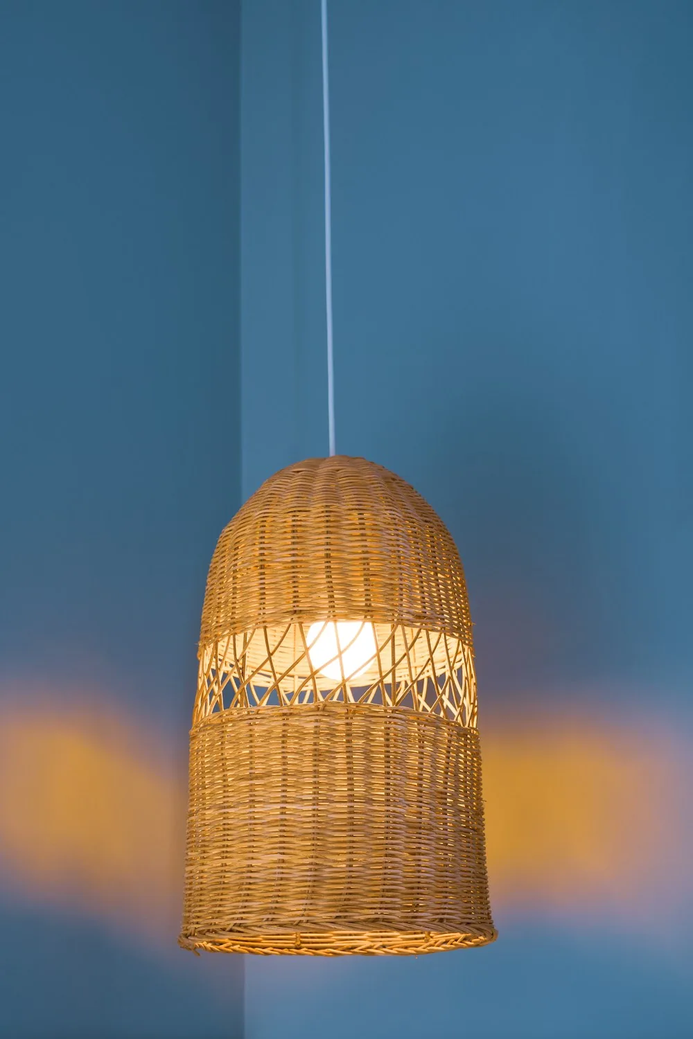 Bell-shaped wicker pendant lamp lit against a blue wall