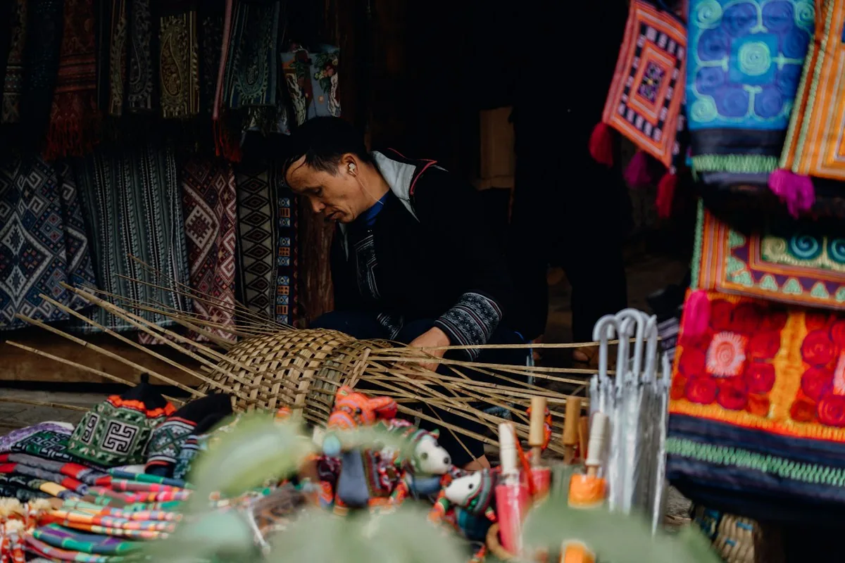 Person weaving a basket among colourful textiles