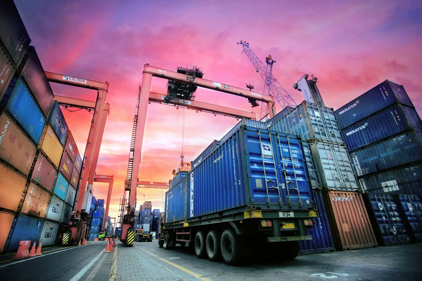 Container truck between stacked shipping containers at sunset